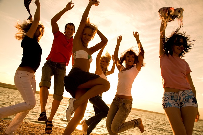 group of happy young people dancing at the beach on beautiful summer sunset