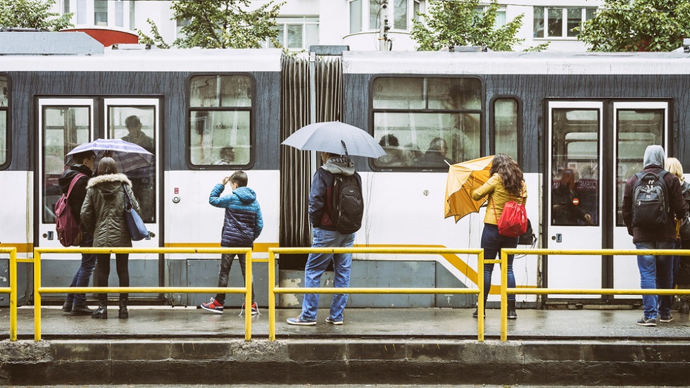 Oameni cu umbrele in statie la tramvai